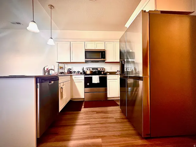 Kitchen featuring wood-finish flooring, white cabinetry, stainless steel appliances, and pendant lighting