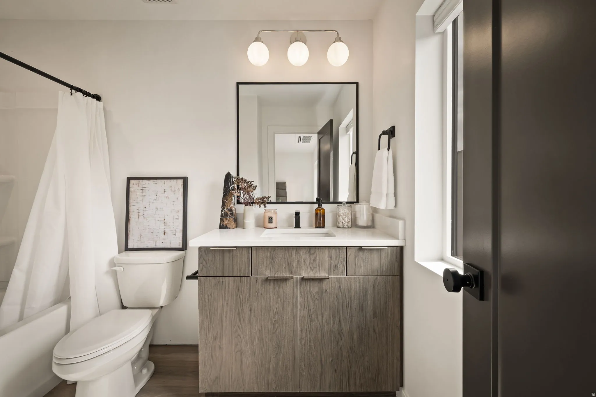 Bathroom featuring a wood-finish vanity with a white countertop and rectangular sink, a black-framed mirror, and a three-light vanity fixture