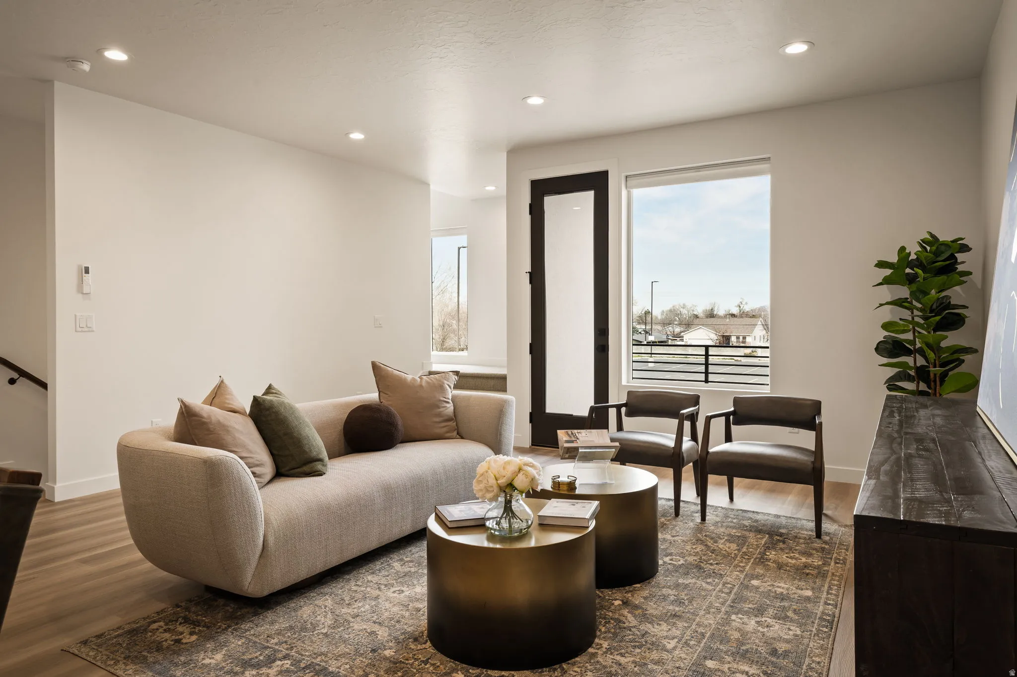 Bright living area featuring recessed lighting, wood-finish flooring, a large window with black framing, and a dark-framed glass paneled door