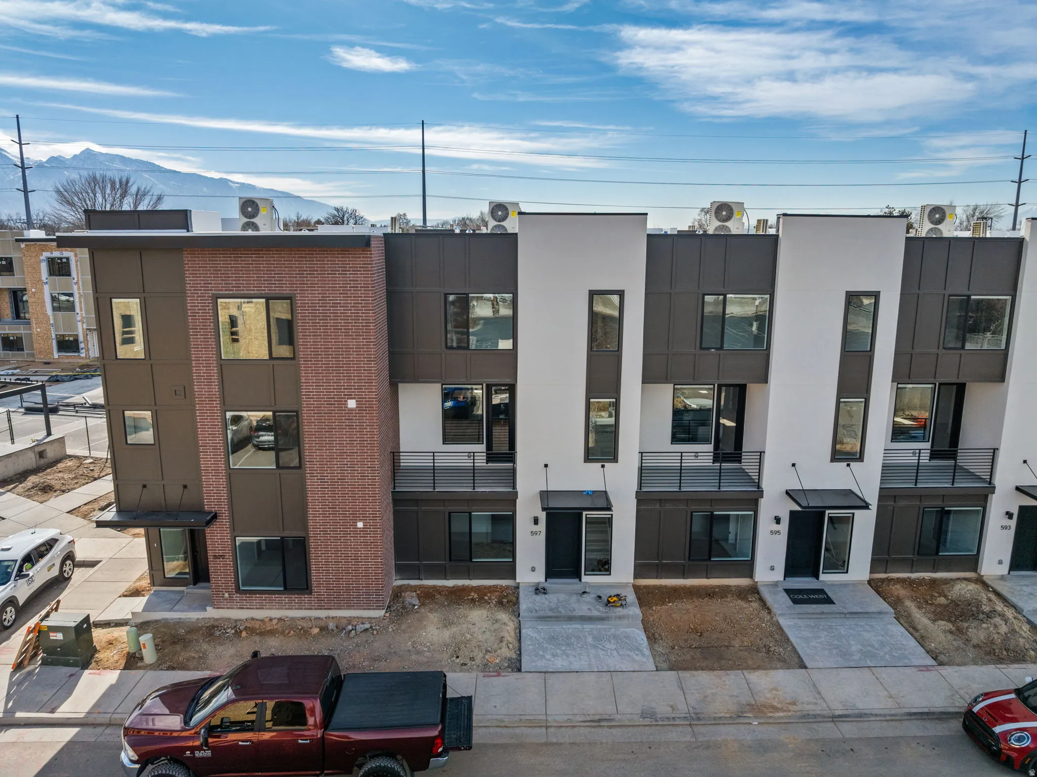 Contemporary townhomes featuring a multi-textured facade with brick, dark paneling, and white stucco