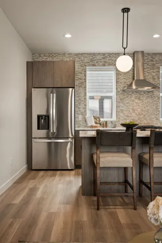 Modern kitchen space featuring stainless steel appliances, wood-finish flooring, recessed lighting, and a textured stone backsplash