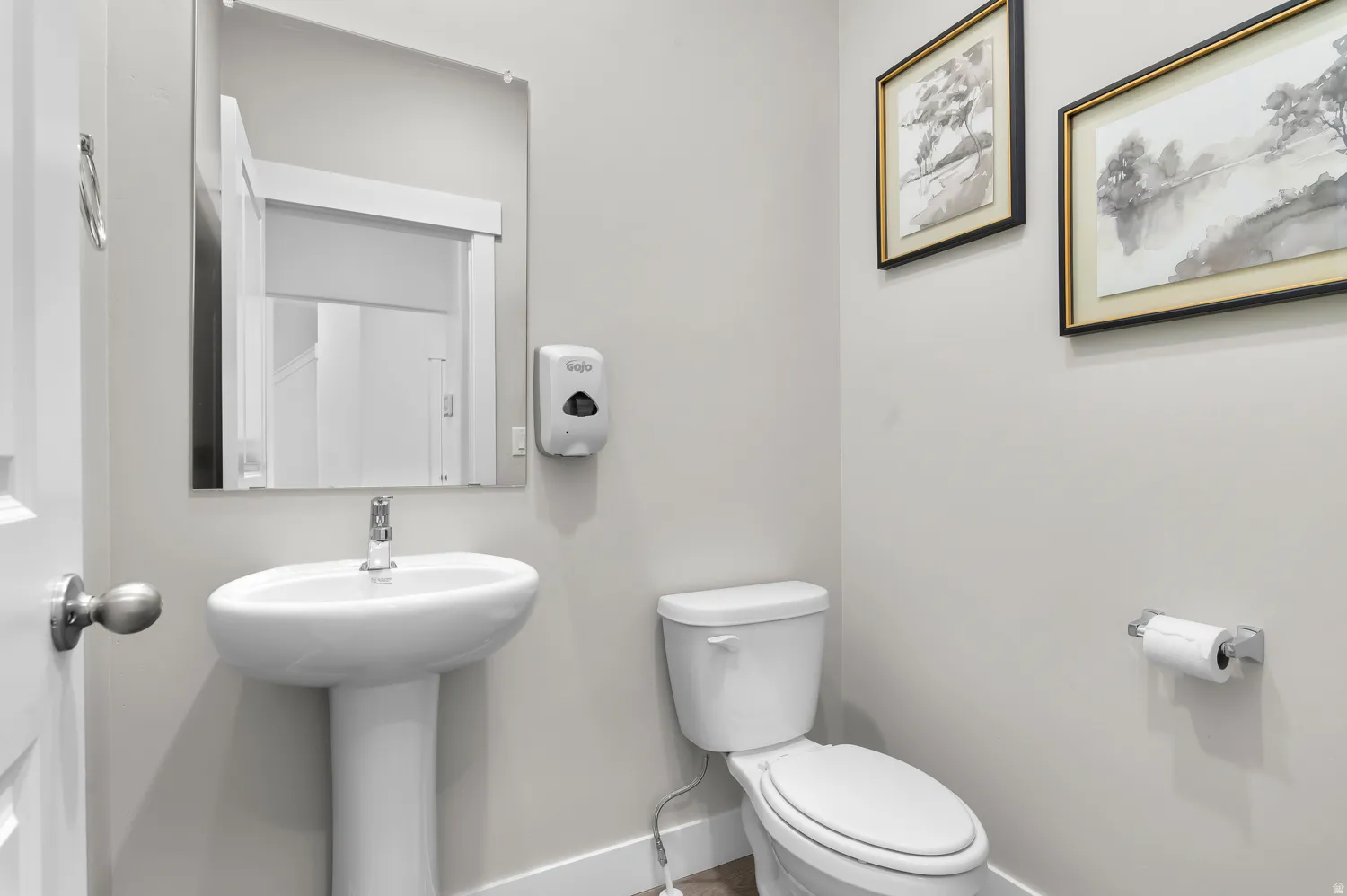 Pedestal sink with chrome faucet, a wall-mounted mirror, and a contemporary toilet