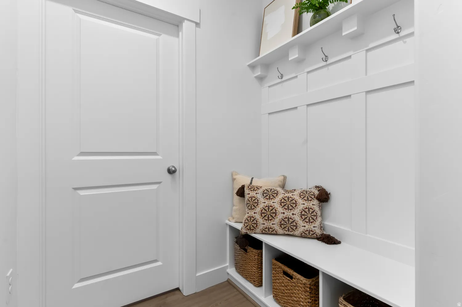 White built-in bench with cubby storage, featuring a board and batten wall with hooks and an overhead shelf