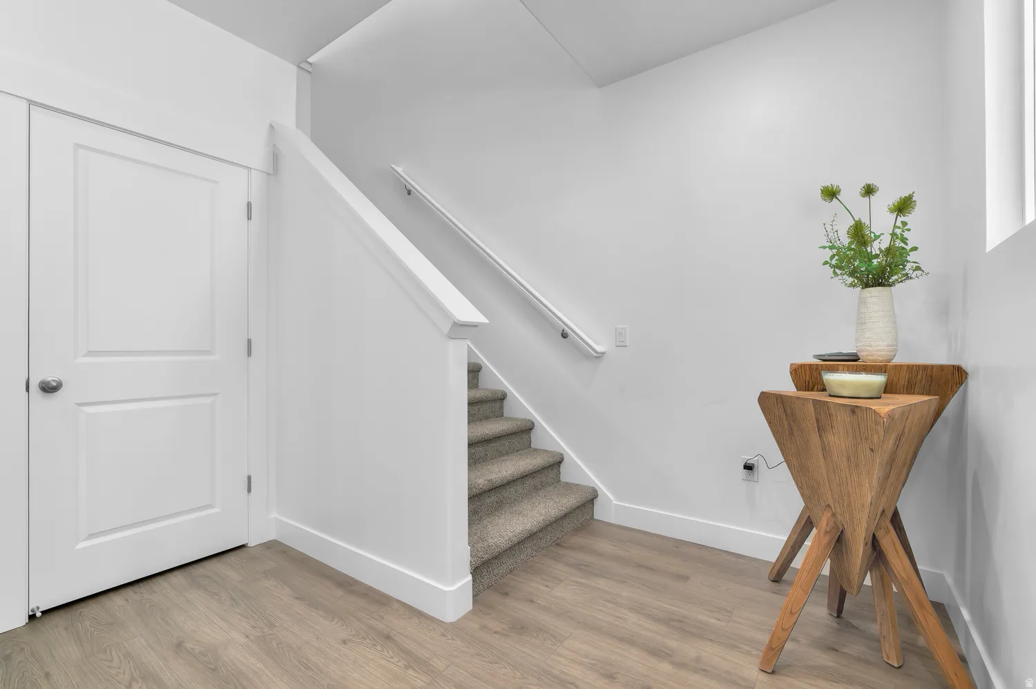 Neutral color palette featuring wood-finish flooring, white trim, a paneled interior door, and carpeted stairs with a white handrail