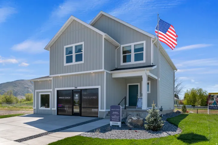 Two-story residence featuring light gray vertical and horizontal siding, a covered front entry with a dark teal door, and a concrete driveway