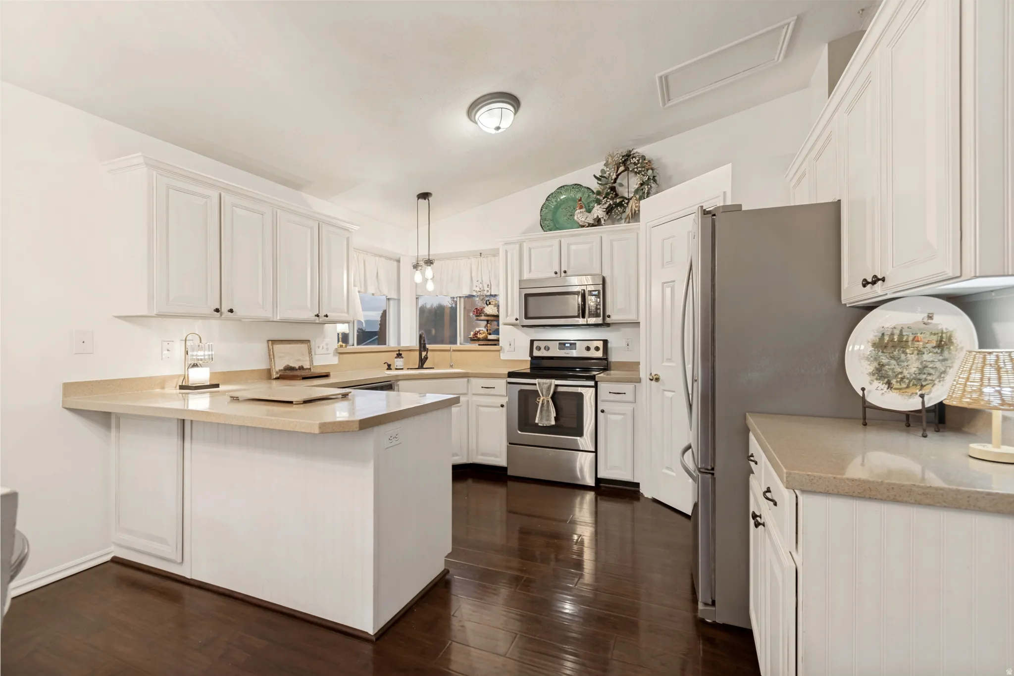 Kitchen featuring white cabinetry, light countertops, wood-finish flooring, stainless steel appliances, and a vaulted ceiling