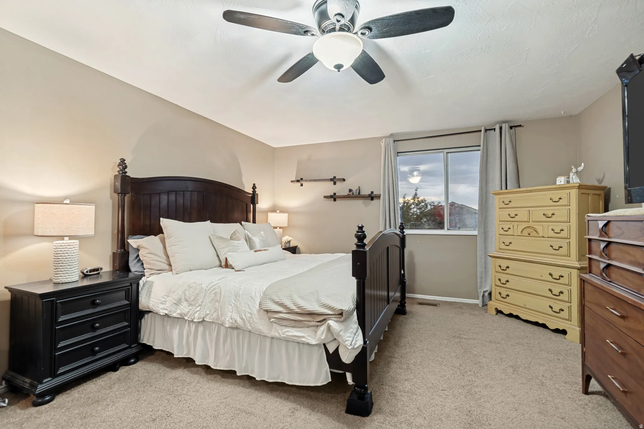 Carpeted room with a ceiling fan, a window with curtains, and wall-mounted shelving