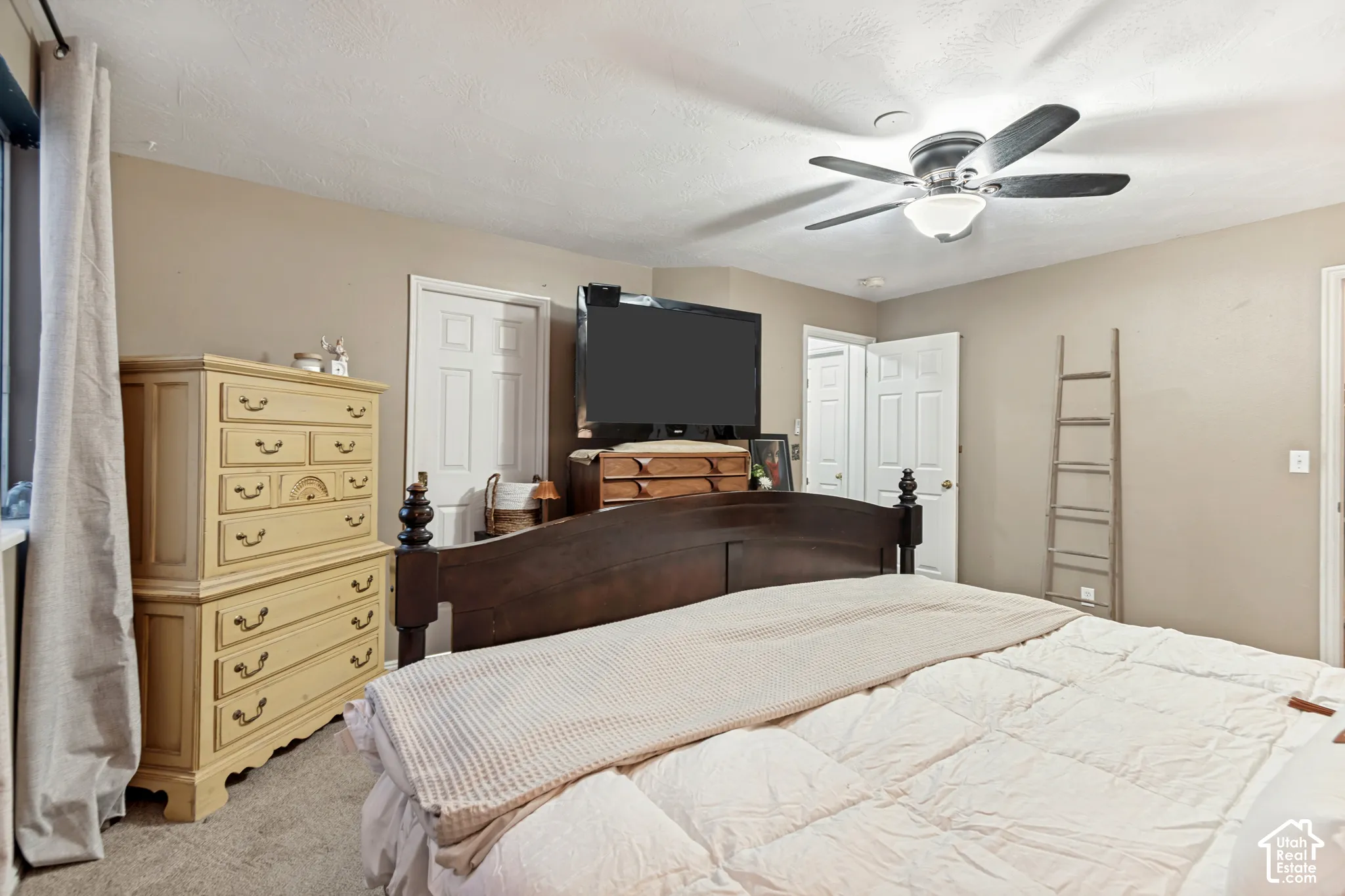 Carpeted room featuring a ceiling fan with integrated lighting, multiple white interior doors, and neutral wall tones