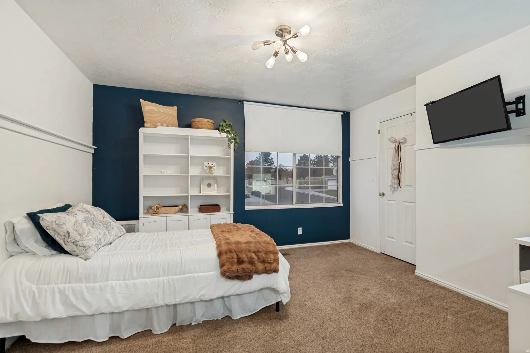 Room featuring a contrasting accent wall, carpeted flooring, a ceiling-mounted light fixture, a window with a roller shade, and a built-in shelving unit