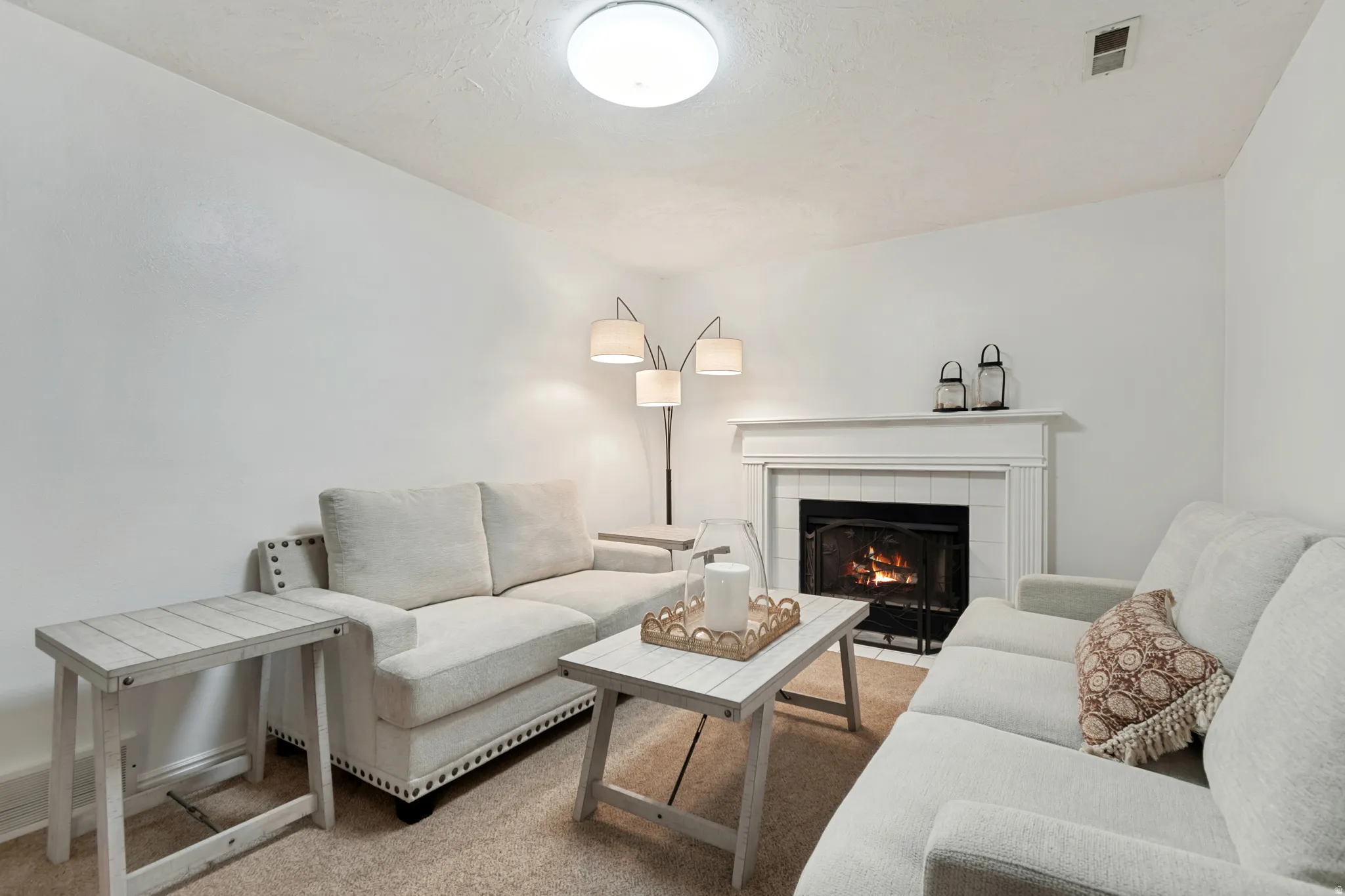 Living area featuring a fireplace with a white mantel and tile surround, recessed firebox, and carpeted flooring