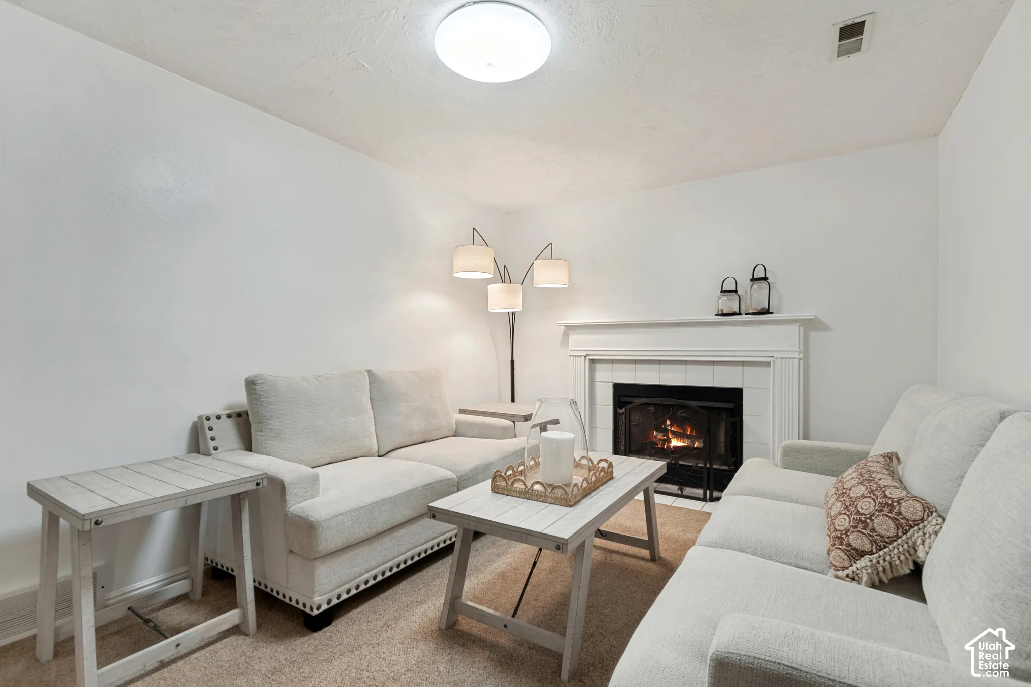 Living area featuring a fireplace with a white mantel and tile surround, recessed firebox, and carpeted flooring