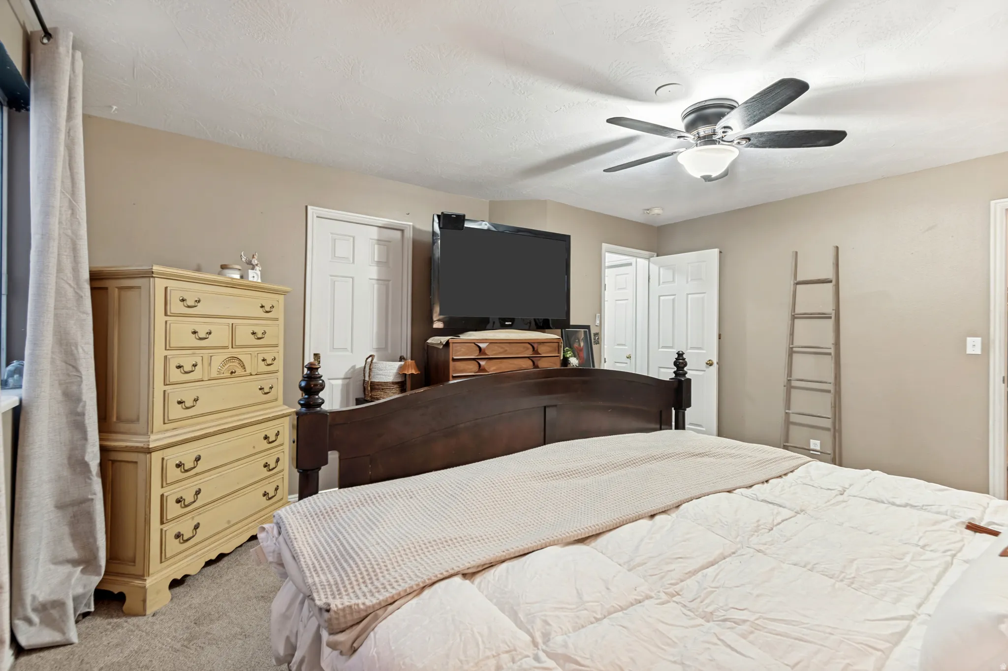 Carpeted room featuring a ceiling fan with integrated lighting, multiple white interior doors, and neutral wall tones