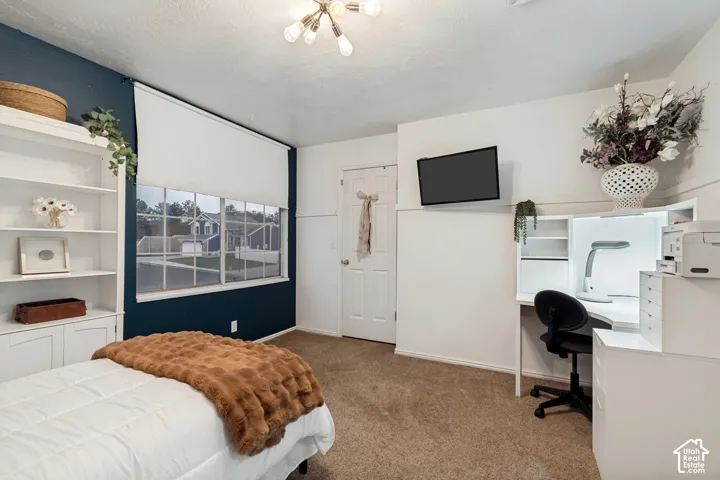 Room featuring a multi-pane window with roller shade, built-in shelving, a recessed desk with integrated lighting, and neutral carpeting