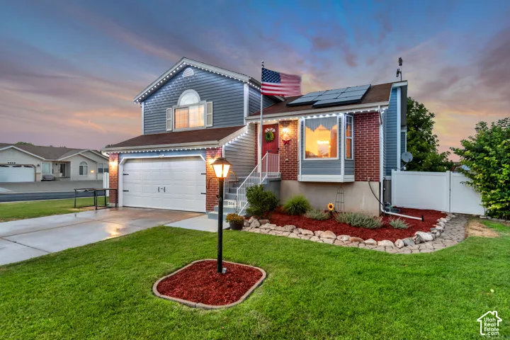Split-level residence featuring a two-car garage, brick and siding exterior, established front lawn, a decorative lamppost, and front landscaping with rock edging