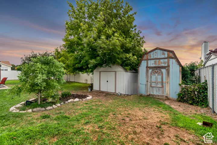 Expansive backyard featuring two sheds, mature trees, a white privacy fence, and a decorative rock-lined planting bed