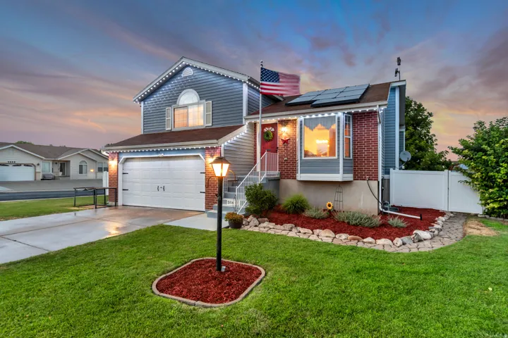 Split-level residence featuring a two-car garage, brick and siding exterior, established front lawn, a decorative lamppost, and front landscaping with rock edging