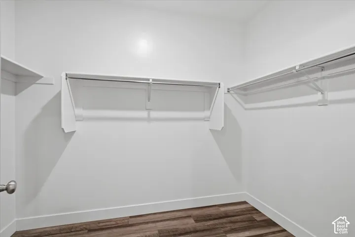 Walk-in closet featuring wood-finish flooring, white walls, white baseboards, and built-in white shelving and hanging rods