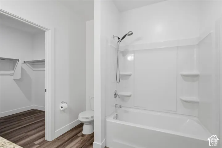 Bathroom featuring a white bathtub with an integrated shower, white walls, and wood-finish flooring