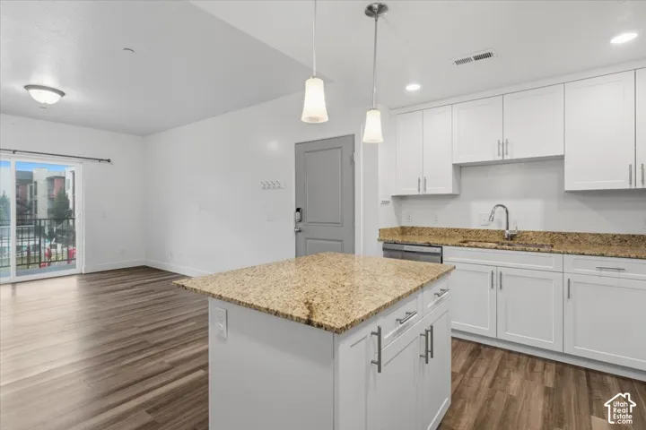 Modern kitchen featuring white cabinetry with brushed nickel hardware, granite countertops, stainless steel appliances, and a central island with pendant lighting