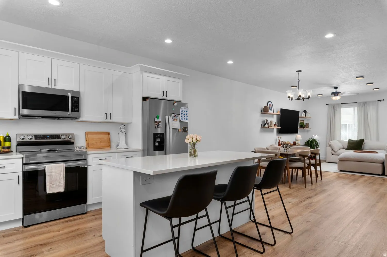 Open-concept kitchen featuring white shaker cabinetry, stainless steel appliances, and a central island with a solid surface countertop