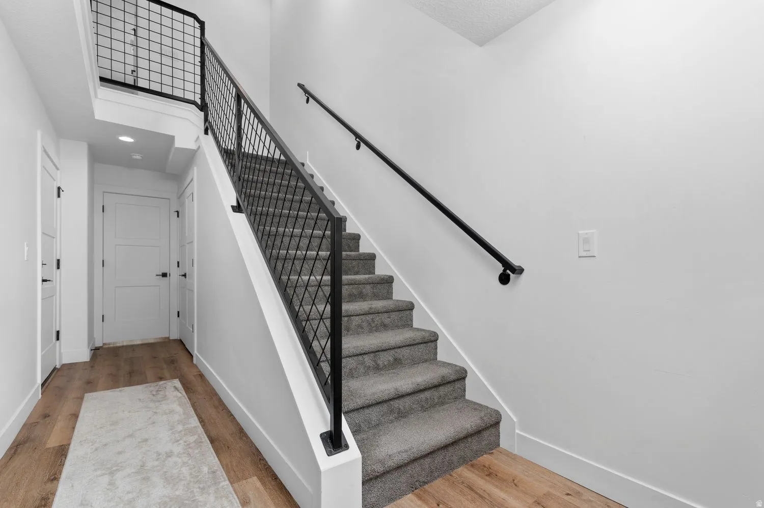 Staircase featuring dark gray carpeted treads, a black metal grid-patterned railing, and a black handrail