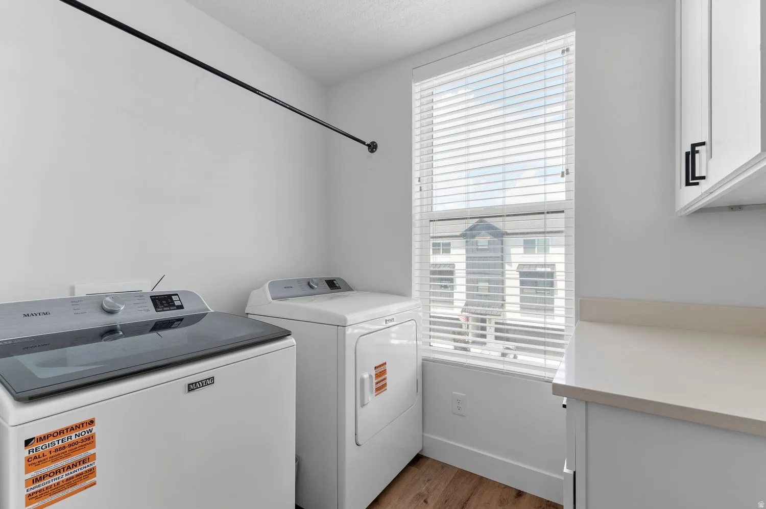Dedicated laundry area featuring a window, wood-finish flooring, white cabinetry, and a countertop