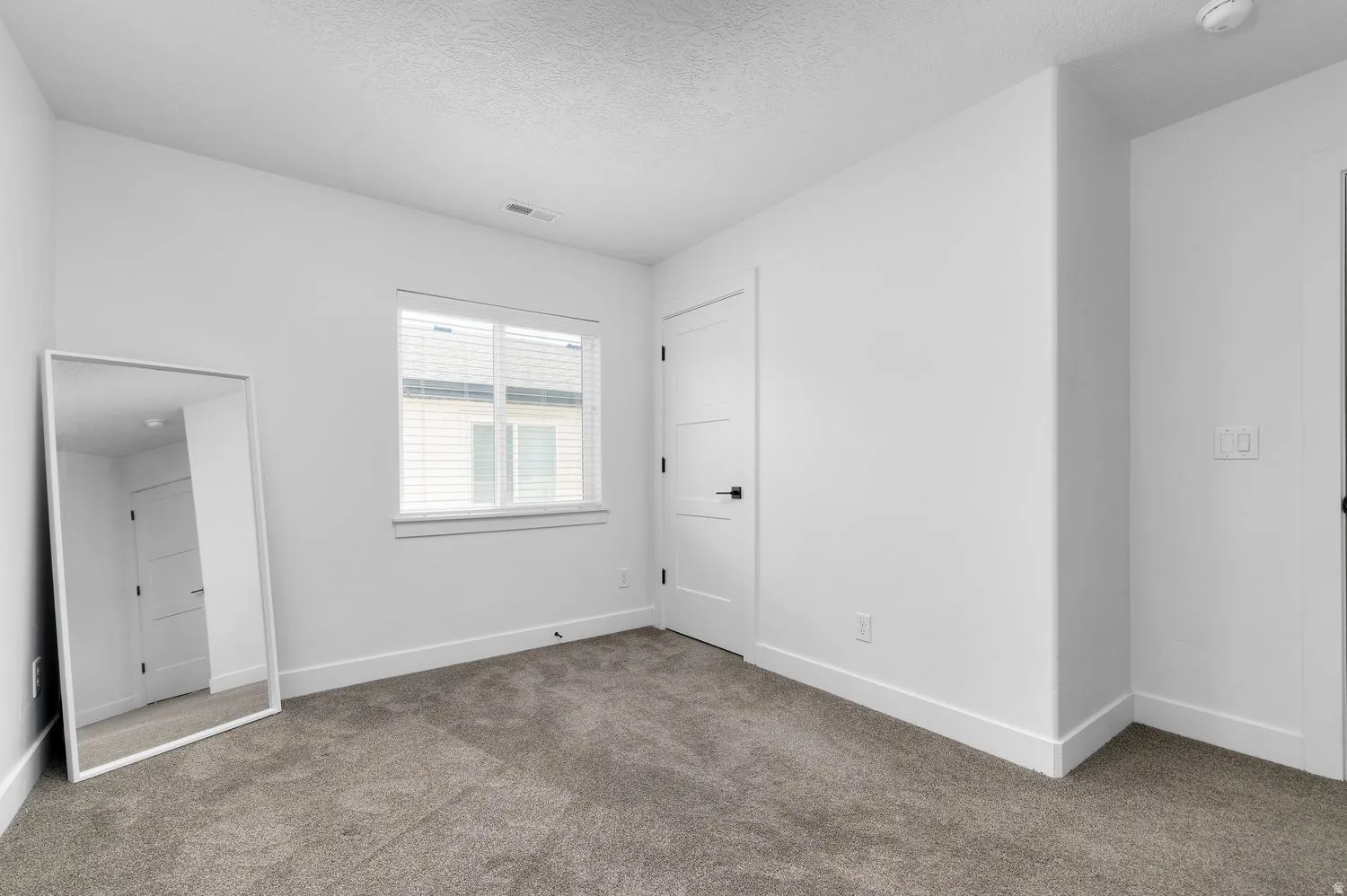 Carpeted room featuring a single window with blinds, white trim, white walls, and a contemporary white panel door