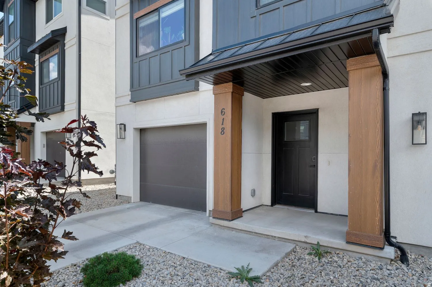 Contemporary exterior with a covered entry featuring wood-finish columns, a dark front door with transom window, and an attached garage