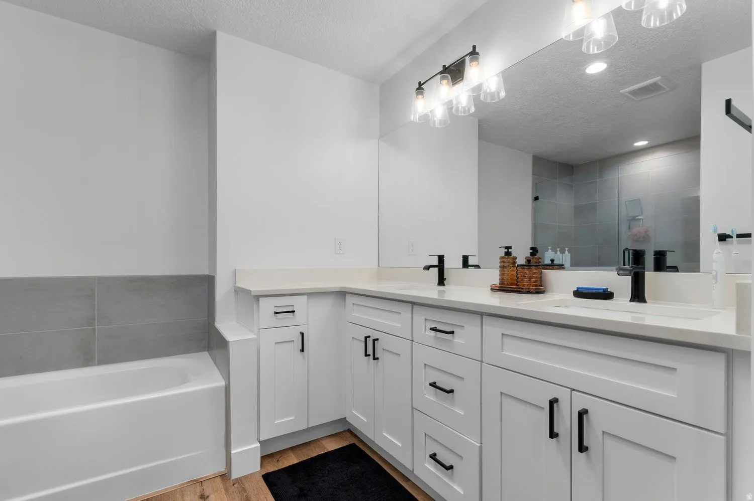 Contemporary bathroom featuring a double vanity with white cabinetry, light-toned countertops, and matte black fixtures