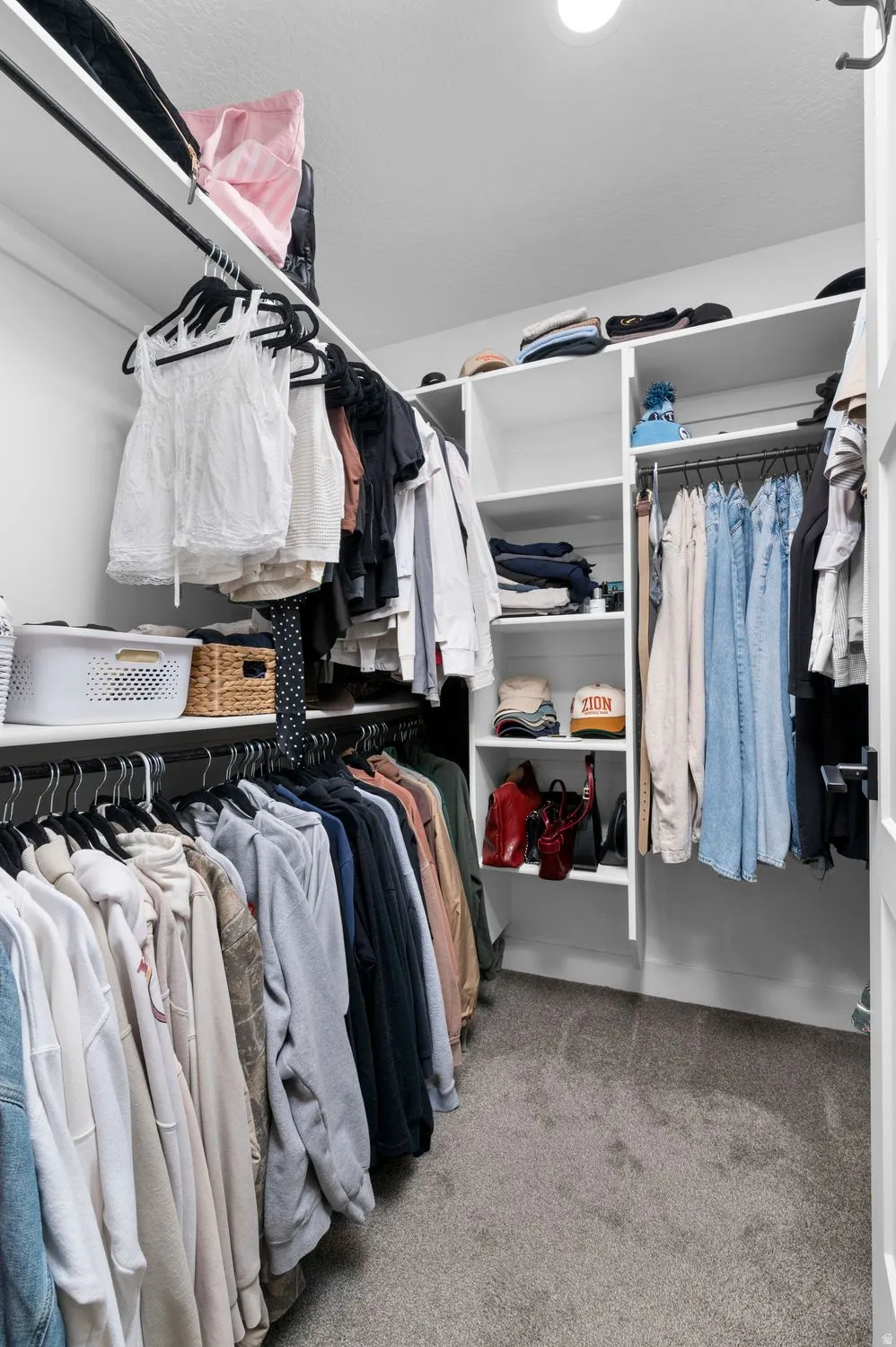 Built-in closet system featuring white shelving, multiple hanging rods, recessed lighting, and grey carpet flooring