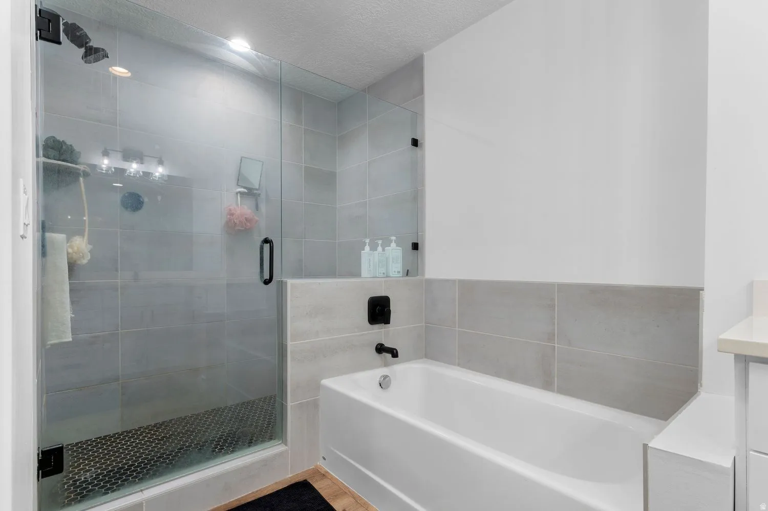 Contemporary bathroom featuring a glass-enclosed shower with dark-finish fixtures, light gray large-format wall tiling, a white soaking tub, and a vanity with a white countertop