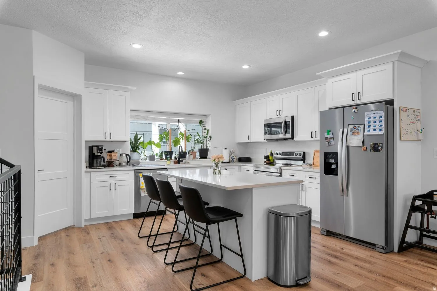 Modern kitchen featuring white shaker cabinetry, stainless steel appliances, a center island with seating, recessed lighting, and wood-finish flooring