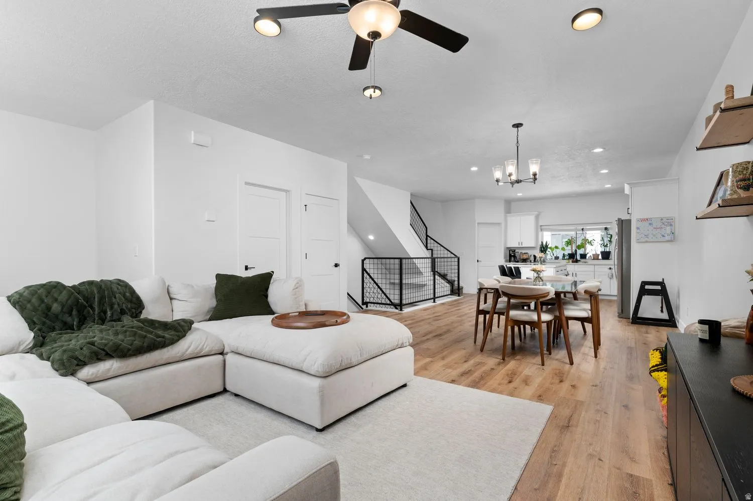 Open-concept living area featuring wood-finish flooring, recessed lighting, a modern ceiling fan, and a staircase with contemporary metal railing