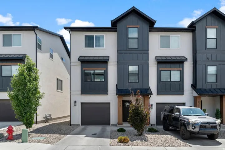Modern multi-story townhouse with a white stucco facade and dark gray vertical siding accents