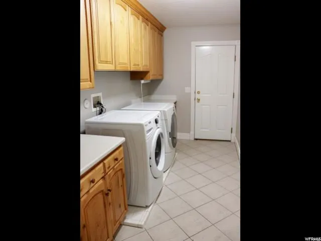 Dedicated laundry area featuring ample cabinetry, a counter surface, and neutral-toned tile flooring