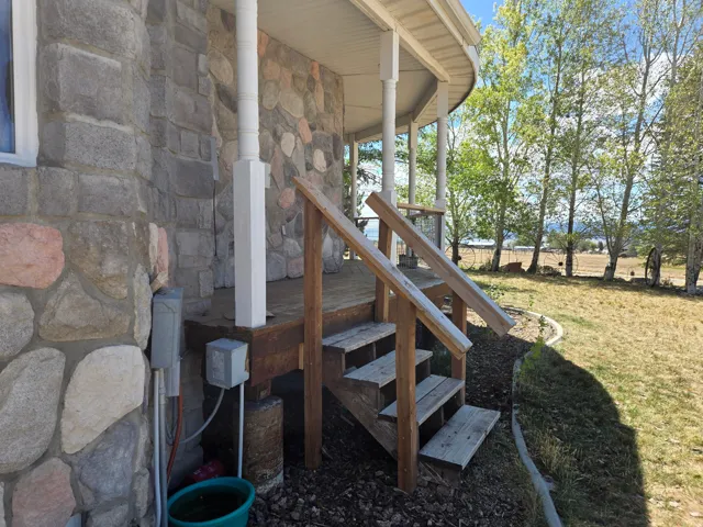 Stone exterior with a covered porch, wood stairs, wood railing, and mature trees