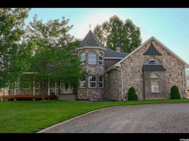 Stone-clad exterior featuring a prominent turret with multiple windows, a covered front porch, and an asphalt shingle roof