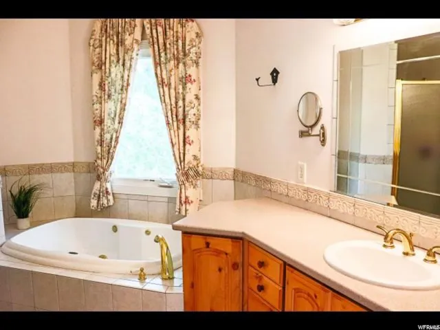 Bathroom featuring a built-in jetted tub with tile surround, a single vanity with wood cabinetry, a light-colored countertop, and a large wall mirror