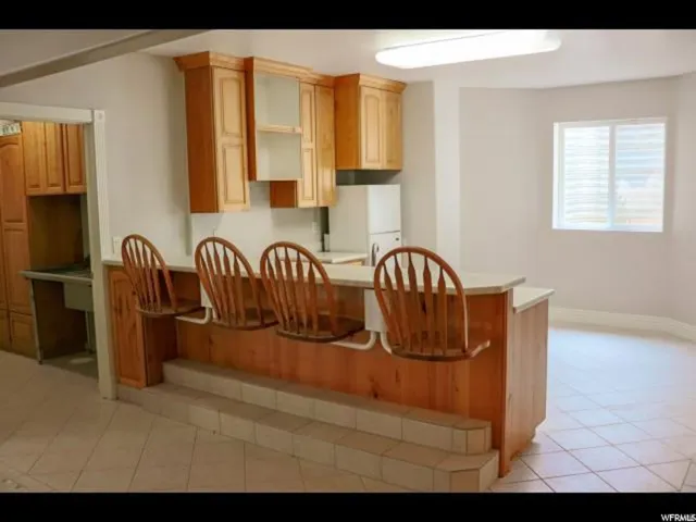 Kitchenette featuring a light wood-finish breakfast bar with integrated seating, wood cabinetry, and a tile floor