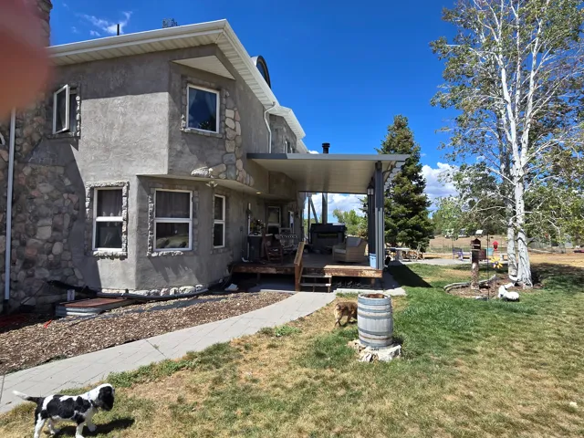 Stucco and stone exterior with multiple windows, a covered outdoor deck, and a paved walkway