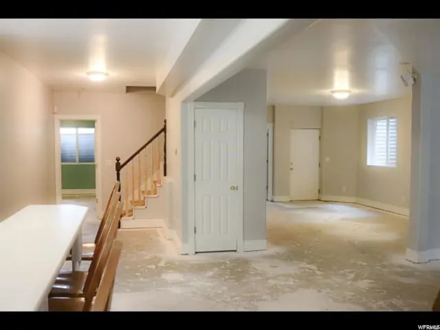 Interior space featuring neutral wall paint, overhead lighting, a visible staircase with wood newel posts and handrail, and a window with white horizontal blinds