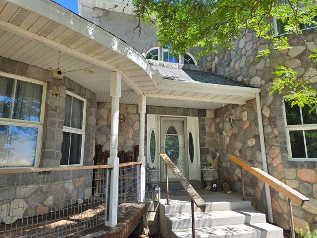 Stone exterior walls, covered front porch, white entry door with oval glass inserts, concrete steps, and a wooden porch railing