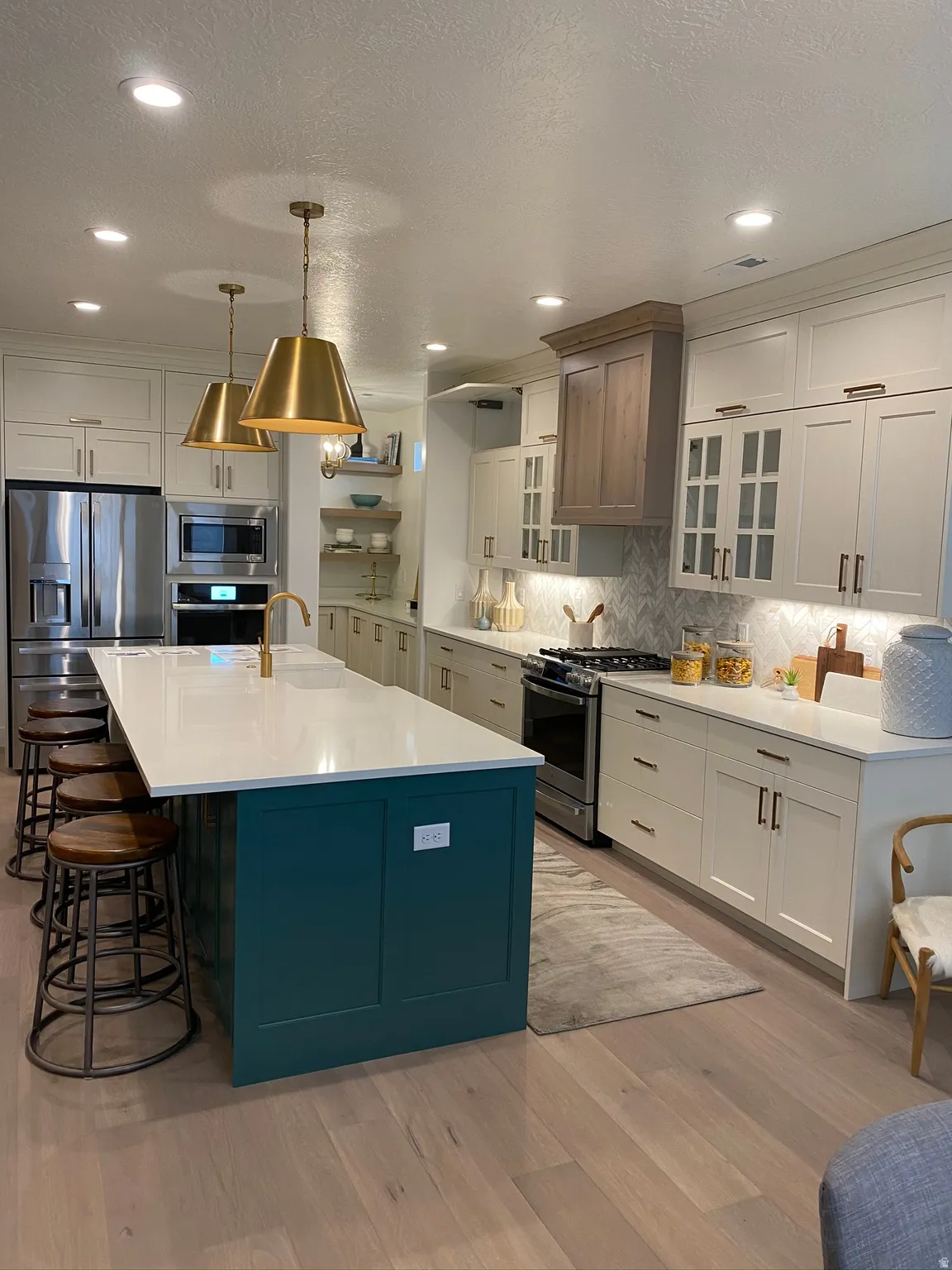 Gourmet kitchen featuring a large central island with a solid surface countertop, light wood-finish flooring, two-tone cabinetry, stainless steel appliances, and recessed lighting