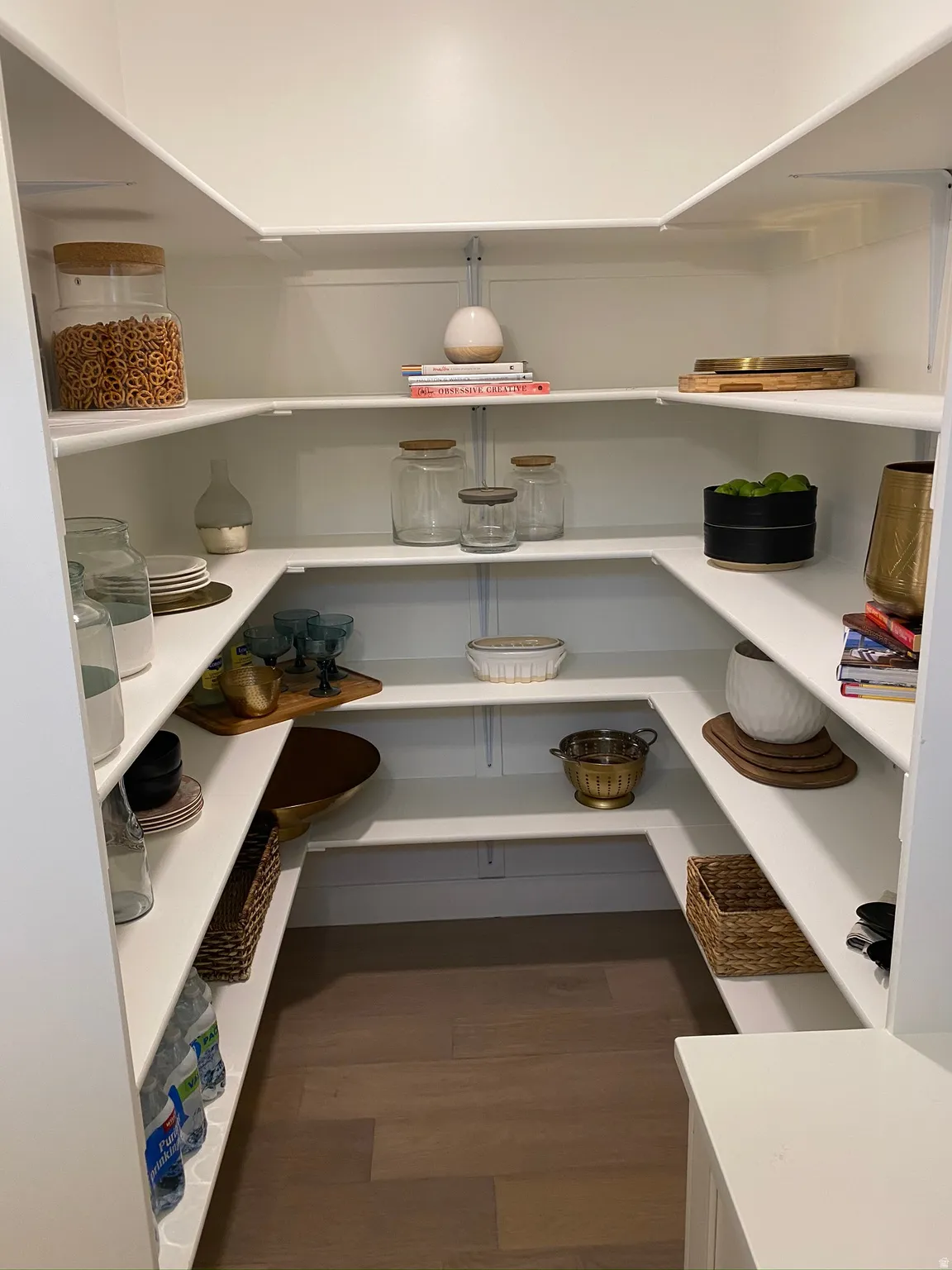 Expansive walk-in pantry featuring white shelving, a wood-finish floor, and ample storage space