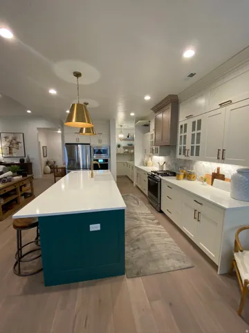Spacious kitchen featuring an expansive central island with a white countertop, light wood-finish flooring, recessed lighting, and dual brass pendant lights