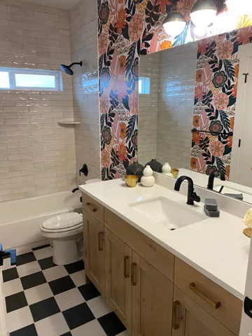 Bathroom featuring a natural wood-finish vanity with a white countertop and integrated sink, black and white checkered floor, and a full-width mirror