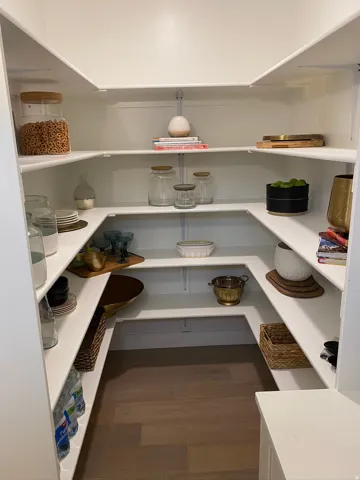 Expansive walk-in pantry featuring white shelving, a wood-finish floor, and ample storage space