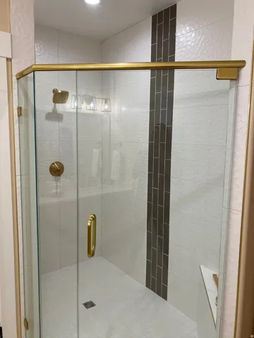 Glass-enclosed shower featuring gold-toned hardware, white patterned wall tiles, a contrasting vertical subway tile accent, a built-in shower bench, and a square-patterned floor tile