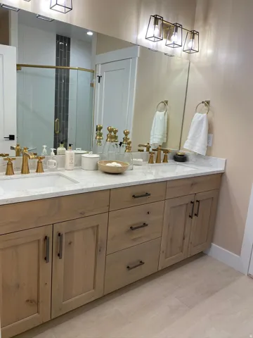 Dual vanity with light wood-finish cabinetry, white countertop, and gold-finish fixtures