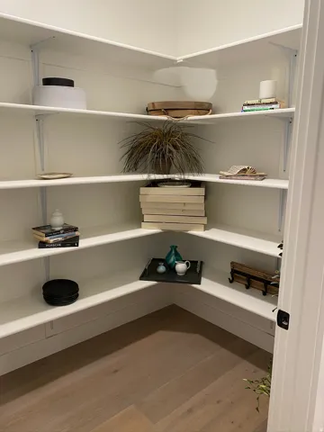 Corner pantry featuring white adjustable shelving, white shiplap wall paneling, and wood-finish flooring